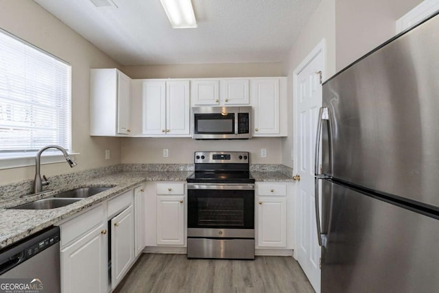 kitchen with sink, light hardwood / wood-style flooring, stainless steel appliances, light stone countertops, and white cabinets