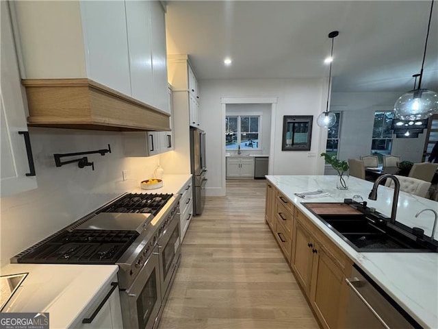 kitchen featuring appliances with stainless steel finishes, sink, white cabinets, hanging light fixtures, and light hardwood / wood-style flooring