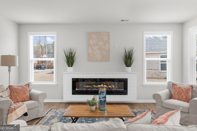 living area with a glass covered fireplace, a healthy amount of sunlight, visible vents, and wood finished floors