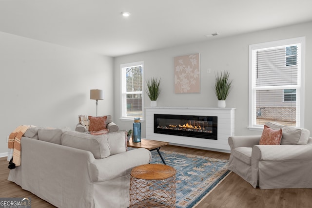 living room with a glass covered fireplace, visible vents, recessed lighting, and wood finished floors