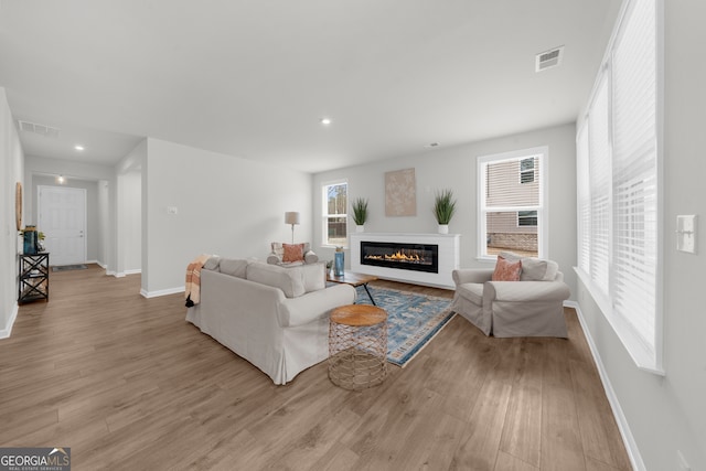 living area featuring a glass covered fireplace, visible vents, baseboards, and wood finished floors