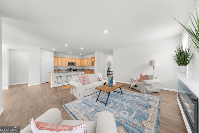 living area featuring baseboards, light wood finished floors, a glass covered fireplace, and recessed lighting