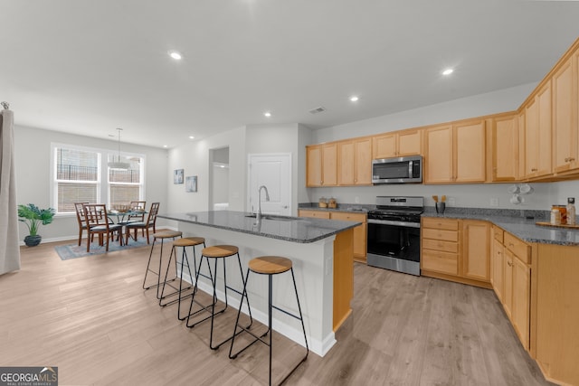 kitchen with light wood finished floors, stainless steel appliances, recessed lighting, light brown cabinetry, and a kitchen breakfast bar