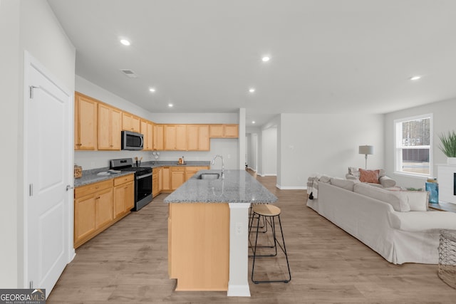 kitchen featuring light brown cabinets, a sink, open floor plan, stainless steel microwave, and range with gas cooktop