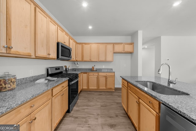 kitchen with light stone counters, stainless steel appliances, a sink, and light brown cabinetry