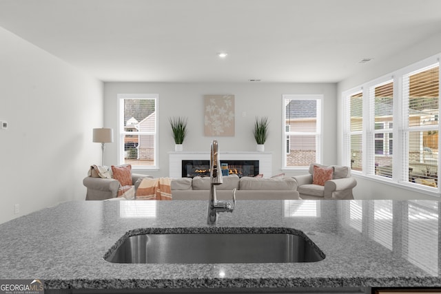 kitchen featuring a glass covered fireplace, dark stone counters, a sink, and visible vents