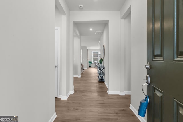 hall with baseboards, visible vents, and wood finished floors