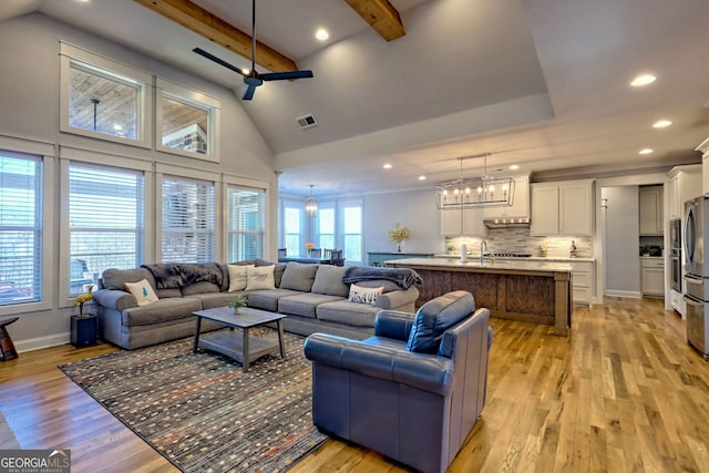 living room with ceiling fan with notable chandelier, high vaulted ceiling, beamed ceiling, and light wood-type flooring