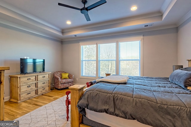 bedroom with a raised ceiling, ceiling fan, and light wood-type flooring