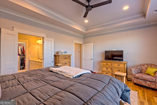 bedroom with a raised ceiling, a walk in closet, ceiling fan, and light hardwood / wood-style flooring