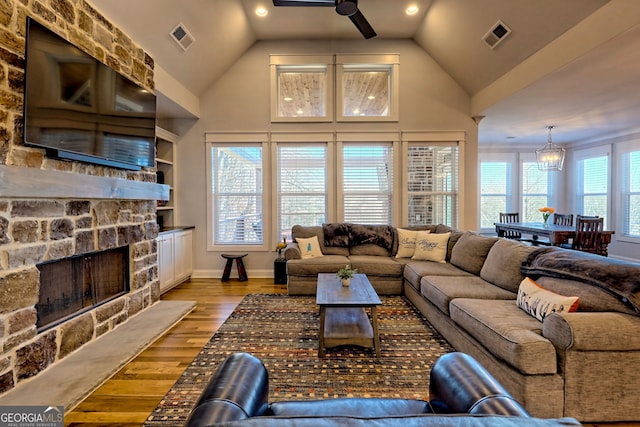 living room featuring hardwood / wood-style floors, a stone fireplace, ceiling fan with notable chandelier, and high vaulted ceiling