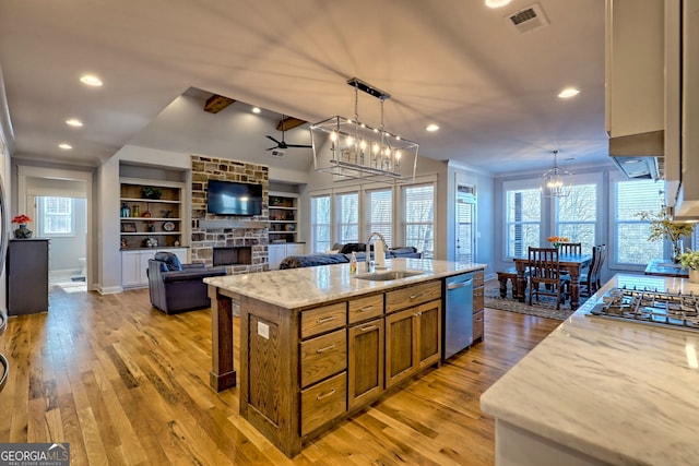 kitchen with sink, light stone counters, hanging light fixtures, stainless steel appliances, and a kitchen island with sink