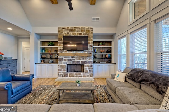 living room featuring a stone fireplace, high vaulted ceiling, built in features, and light wood-type flooring