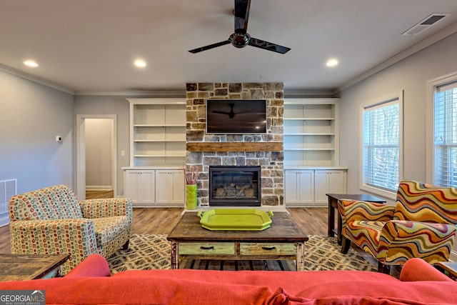 living room with a fireplace, ornamental molding, ceiling fan, light hardwood / wood-style floors, and built in shelves