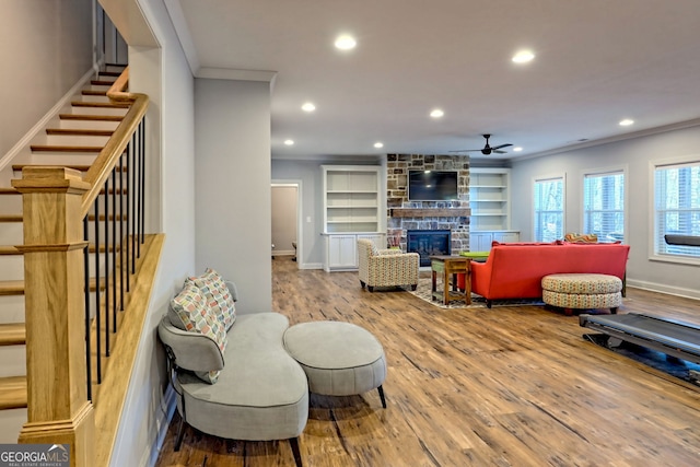 living room with built in features, ornamental molding, a stone fireplace, and wood-type flooring