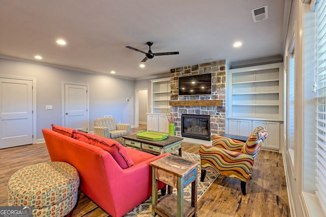 living room with crown molding, a stone fireplace, and light hardwood / wood-style floors