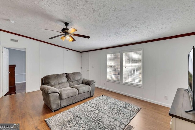 living room with a textured ceiling, wood-type flooring, ornamental molding, and ceiling fan