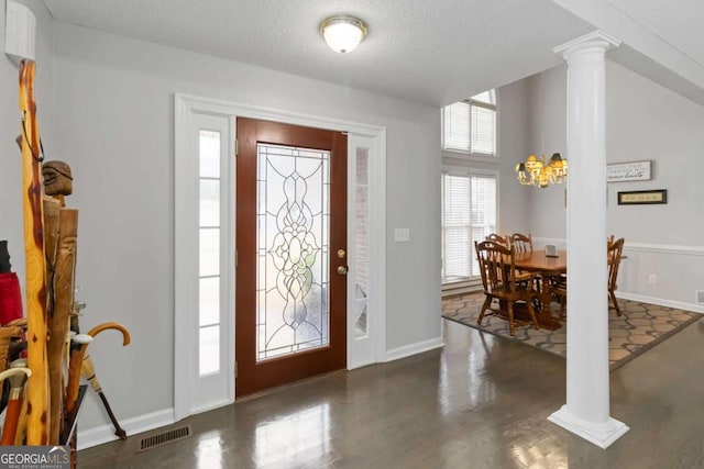 foyer entrance with decorative columns, dark wood-type flooring, a notable chandelier, and a textured ceiling