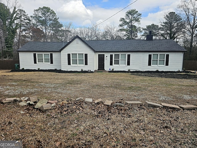 ranch-style home with a shingled roof, a chimney, and a front lawn