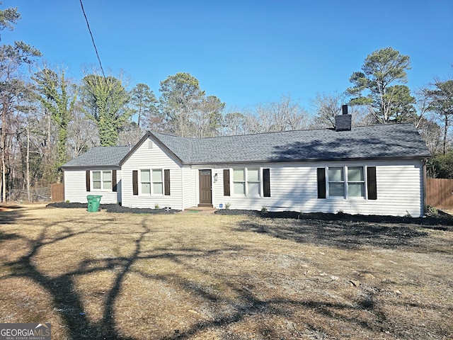 ranch-style house with a shingled roof, a chimney, and a front yard