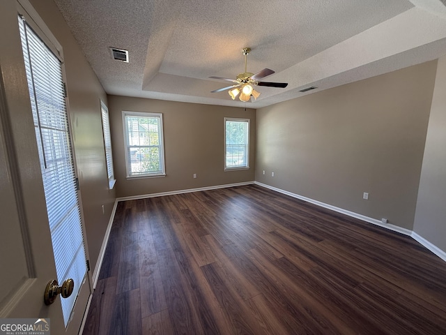 spare room with a textured ceiling, dark wood finished floors, baseboards, a ceiling fan, and a raised ceiling