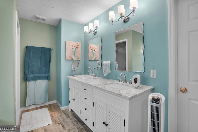 full bathroom featuring wood finished floors, a textured ceiling, baseboards, and double vanity