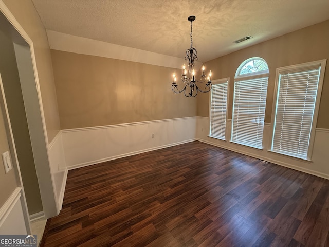 unfurnished room featuring a chandelier, dark wood-style floors, a textured ceiling, and a wainscoted wall