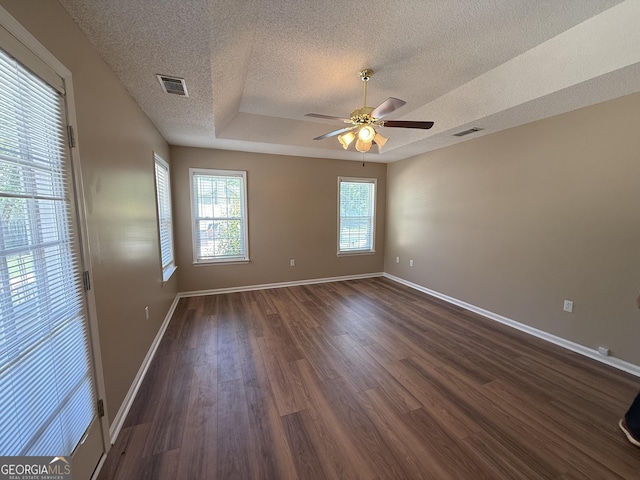 empty room with a textured ceiling, plenty of natural light, dark wood-type flooring, a ceiling fan, and baseboards
