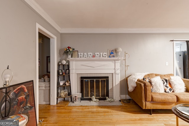 living area with ornamental molding, a brick fireplace, and wood finished floors