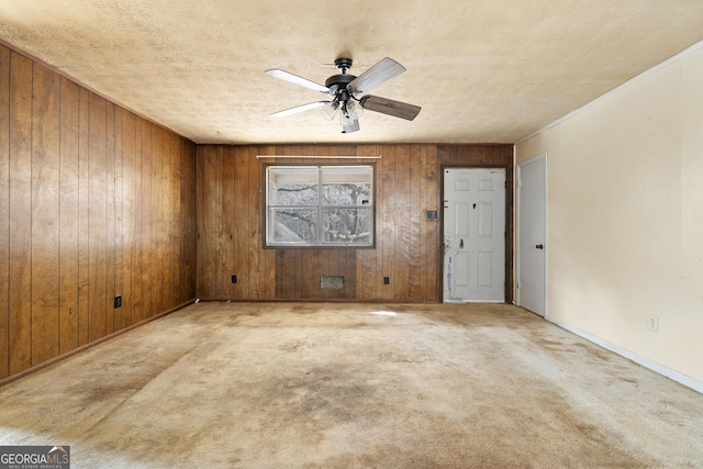 carpeted spare room with ceiling fan, wooden walls, and a textured ceiling