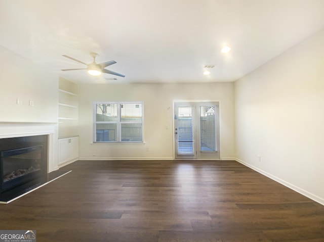 unfurnished living room with ceiling fan, dark hardwood / wood-style floors, and built in shelves