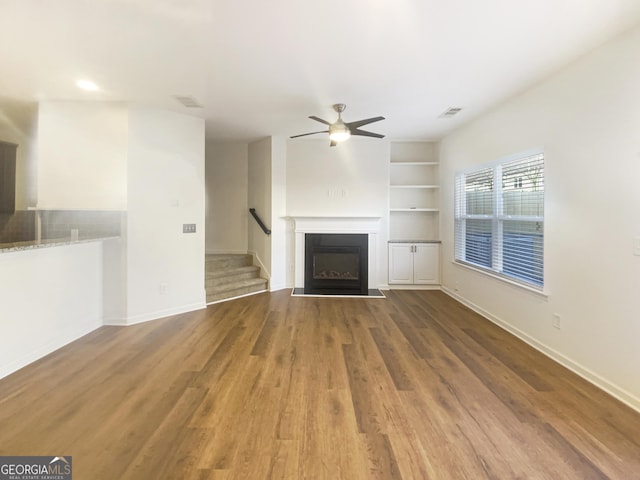 unfurnished living room featuring hardwood / wood-style flooring, ceiling fan, and built in shelves