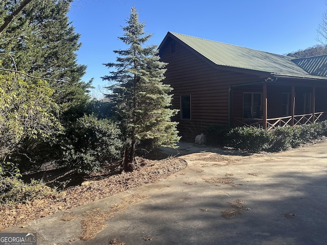 view of side of property featuring a porch, metal roof, and log veneer siding