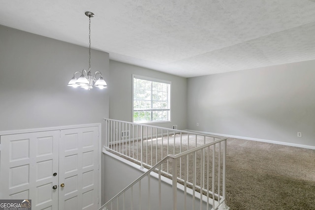 hallway with an inviting chandelier, carpet floors, and a textured ceiling