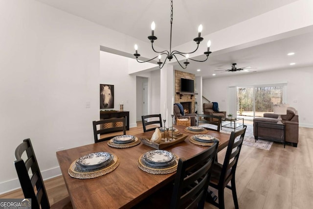 dining space featuring ceiling fan with notable chandelier, a fireplace, and light wood-type flooring