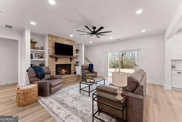 living room with built in shelves, a fireplace, light hardwood / wood-style floors, and ceiling fan