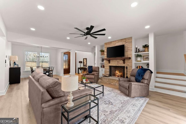 living room featuring ceiling fan with notable chandelier, built in features, a fireplace, and light hardwood / wood-style flooring