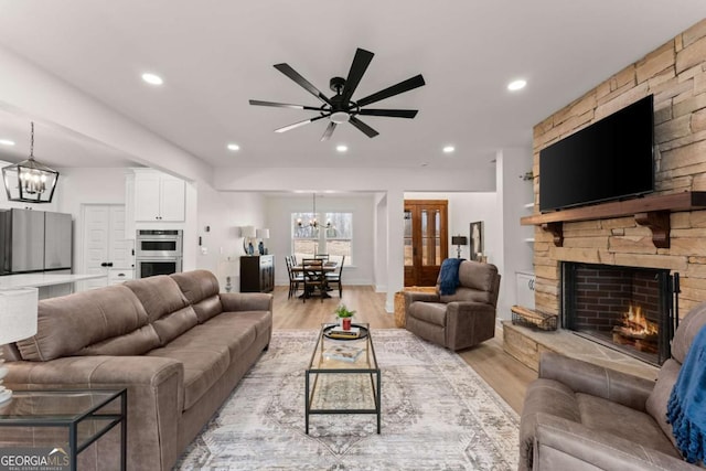 living room with a stone fireplace, ceiling fan with notable chandelier, and light hardwood / wood-style flooring