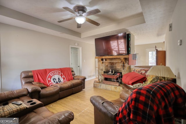 living area featuring a textured ceiling, ceiling fan, a tray ceiling, and wood finished floors