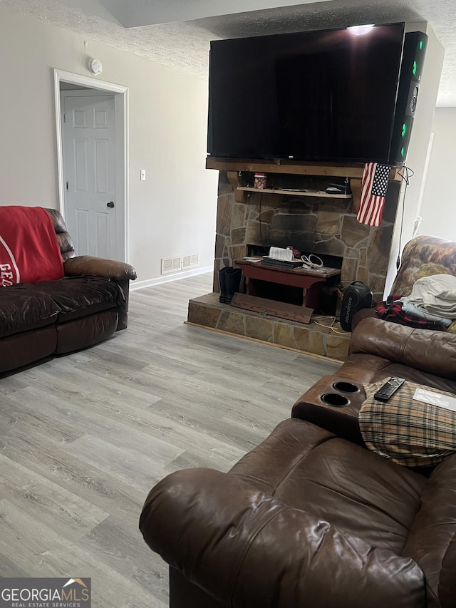 living room with baseboards, visible vents, wood finished floors, a textured ceiling, and a fireplace