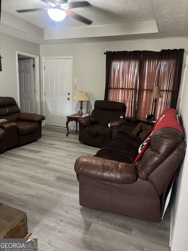 living area with a textured ceiling, ceiling fan, wood finished floors, and a raised ceiling