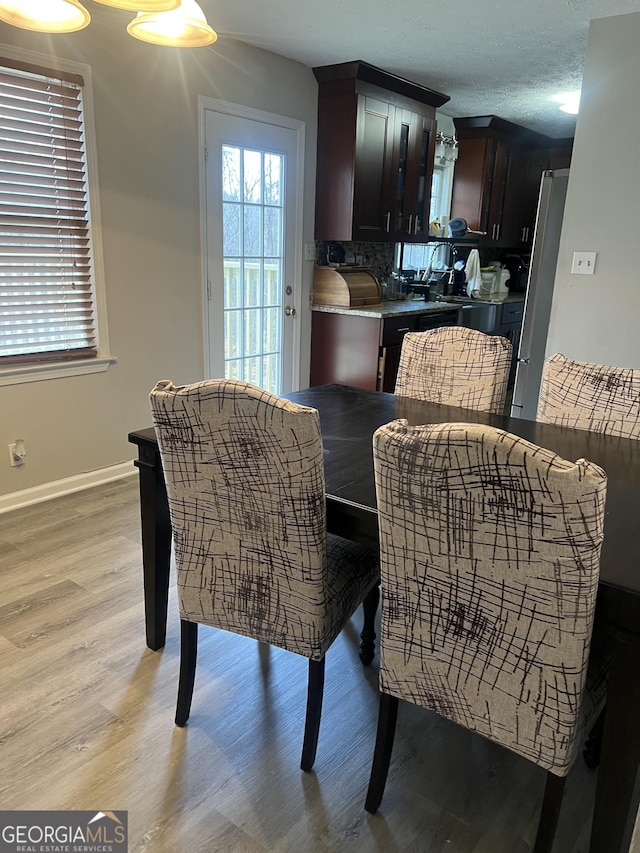 dining space with a textured ceiling, light wood-type flooring, and baseboards