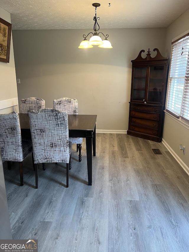 dining area featuring visible vents, a notable chandelier, baseboards, and wood finished floors