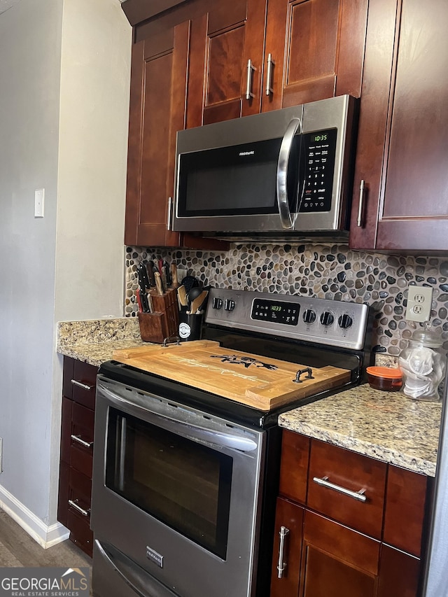 kitchen featuring baseboards, appliances with stainless steel finishes, dark wood-type flooring, light stone countertops, and backsplash