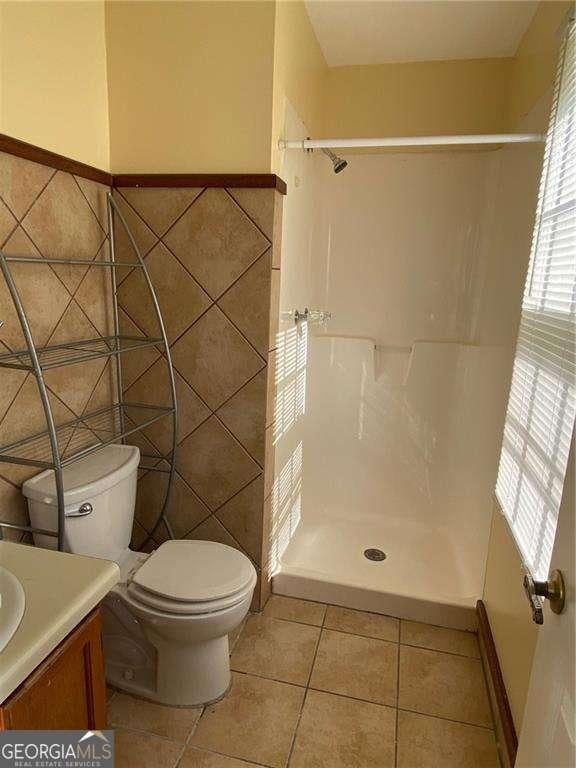 bathroom with a shower, tile walls, tile patterned flooring, vanity, and toilet