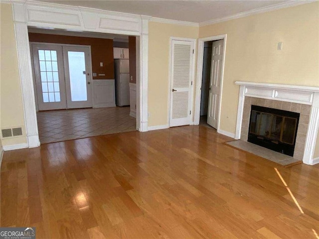 unfurnished living room featuring french doors, ornamental molding, wood-type flooring, and a tiled fireplace