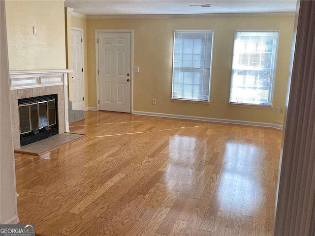 unfurnished living room featuring ornamental molding, a tiled fireplace, and light hardwood / wood-style floors