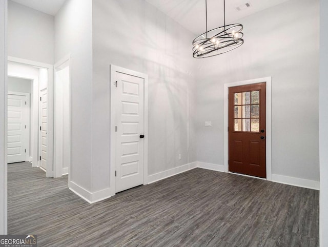 entrance foyer with an inviting chandelier, a towering ceiling, and dark wood-type flooring