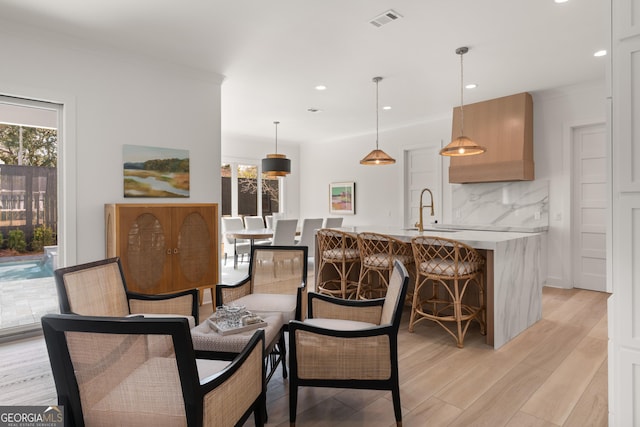 dining room featuring ornamental molding, a wealth of natural light, sink, and light wood-type flooring