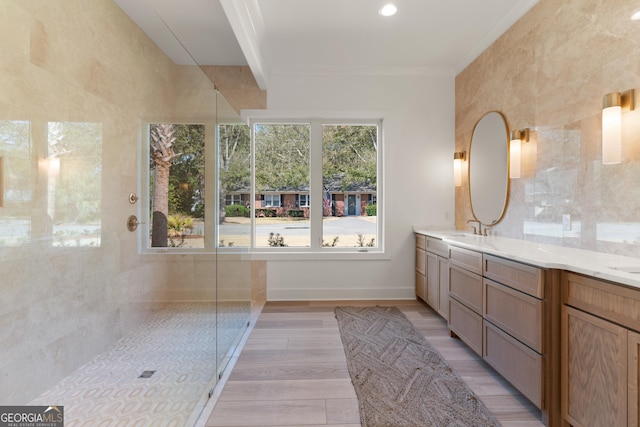 bathroom featuring a tile shower, wood-type flooring, tile walls, ornamental molding, and vanity